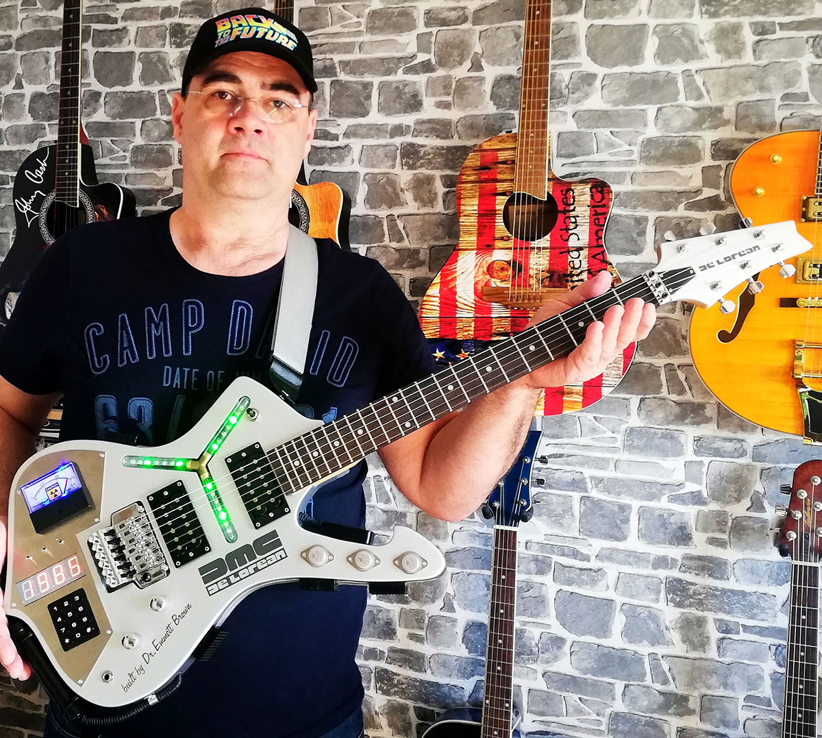 Thomas mit der von ihm umgebauten Gitarre im Back-to-the-Future-Design. Im Hintergrund sieht man weitere außergewöhnliche Gitarren an der Wand hängen.