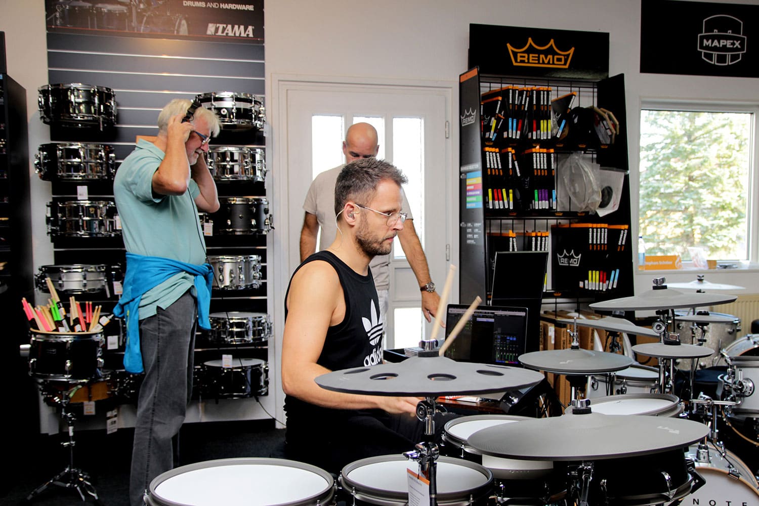 Mitarbeiter der Firma Efnote in der Drumabteilung des Musikhaus Kirstein bei der MusiConnect 2024. Ralf Schumacher an einem E-Drum-Set. Ein Gast setzt sich Kopfhörer auf.